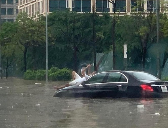 Người đàn ông đứng trên xế hộp Mercedes hơn 2 tỷ để check-in. Xung quanh anh mênh mông nước, mực nước đã ngập qua bánh xe ô tô. 