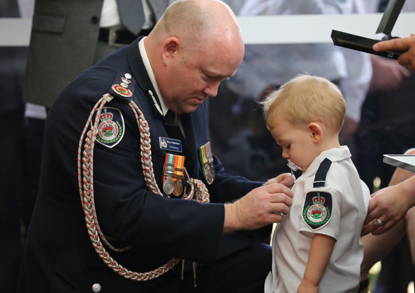 Ông Shane Fitzsimmons, chỉ huy Sở Cứu hỏa bang New South Wales cài huân chương danh dự lên áo của cậu bé Harvey Keaton (19 tháng tuổi) thay mặt cha - trong lễ tang của cha cậu ở phía tây thành phố Sydney hôm 2/1. - Ảnh: AFP