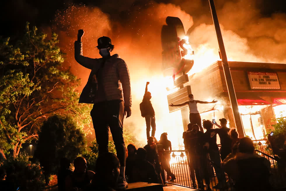 Minneapolis, ngày 29/5/2020. Người biểu tình bên ngoài một nhà hàng thức ăn nhanh đang cháy, bốn ngày sau khi George Floyd bị giết. Các doanh nghiệp trên khắp đất nước chịu thiệt hại do nạn cướp bóc và đốt phá trên diện rộng. Ảnh: John Minchillo/Associated Press