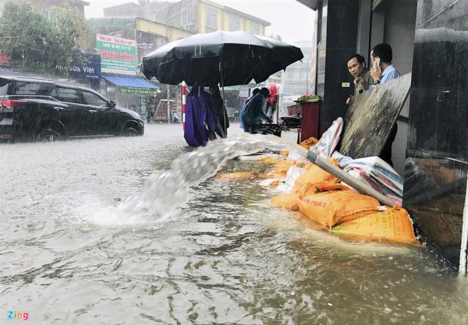 Để tránh nước mưa tràn vào nhà gây ngập, nhiều gia đình sử dụng các tấm chắn và túi cát chắn ngang cửa. Họ còn dùng máy bơm đẩy nước trong nhà ra ngoài. (Ảnh: Zing).